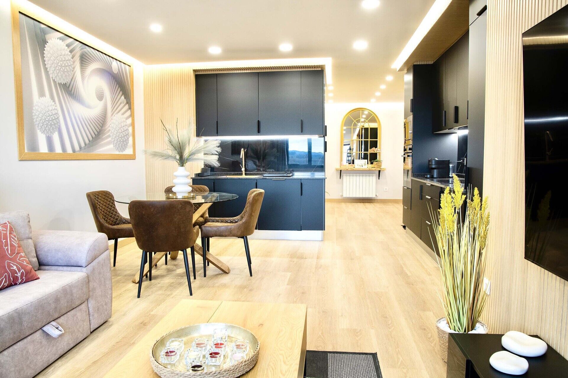 Uma sala de estar moderna com sofá, mesa de jantar com cadeiras, área de cozinha com armários e uma janela grande.