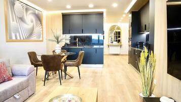 Uma sala de estar moderna com sofá, mesa de jantar com cadeiras, área de cozinha com armários e uma janela grande.