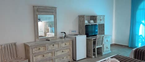 Habitación de hotel con cómoda de madera, escritorio, silla, cama y ventilador de techo.