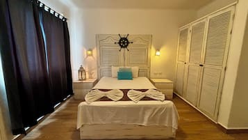 Une chambre à coucher bien rangée, avec un lit, des tables de chevet, une tête de lit ornée d’un volant de navire et une armoire.