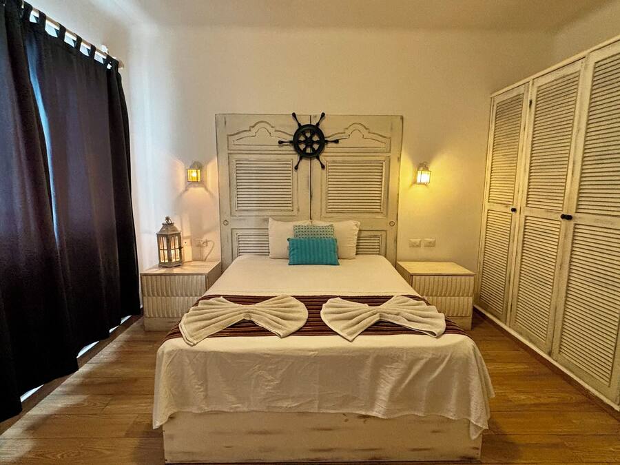 Une chambre à coucher bien rangée, avec un lit, des tables de chevet, une tête de lit ornée d’un volant de navire et une armoire.