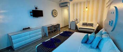 Un dormitorio moderno con cama, escritorio, sofá, televisor y ventilador de techo.