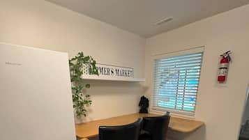 A compact kitchen with a white refrigerator, a wooden countertop, two black chairs, a potted plant, and a window with blinds.