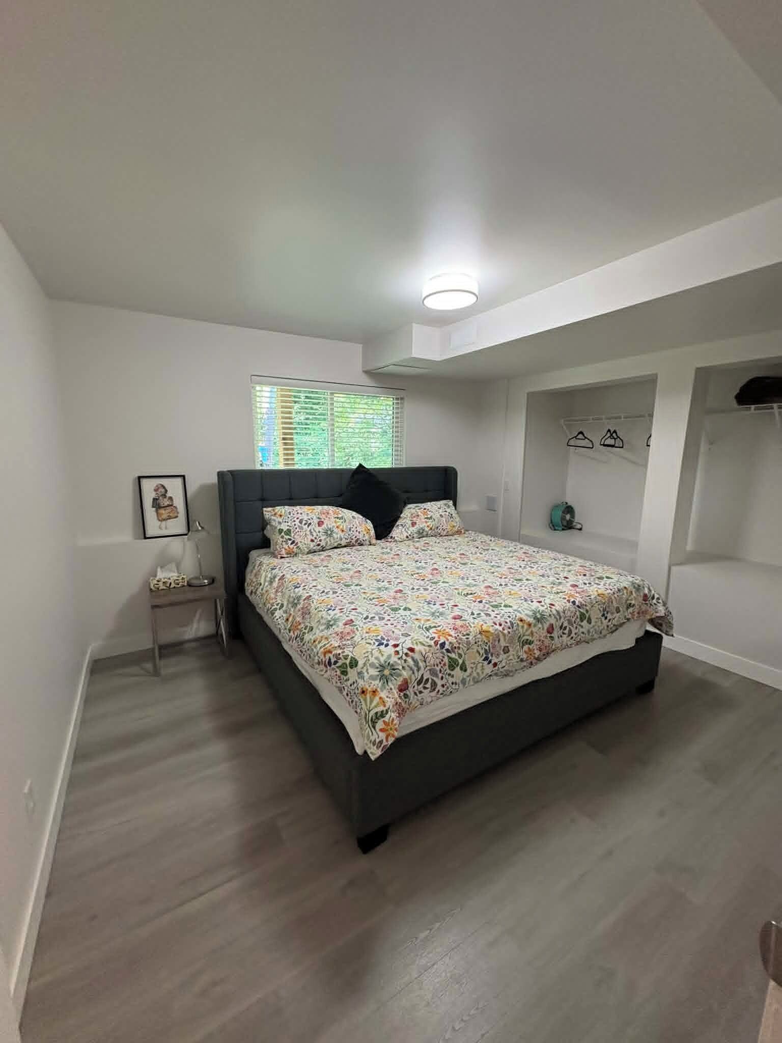 A bedroom with a bed, a nightstand, a window with blinds, and a ceiling light.