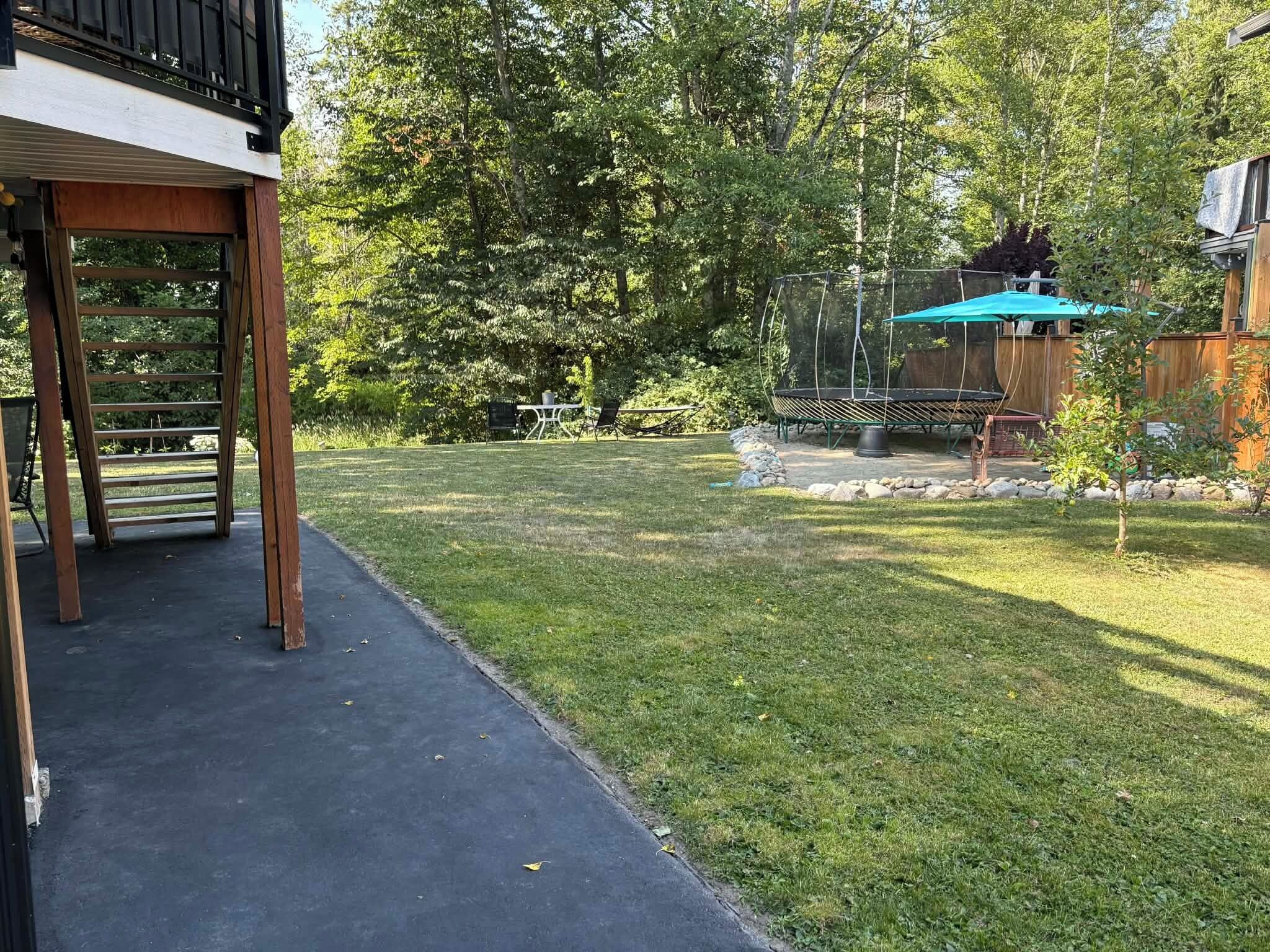A backyard with a trampoline, a wooden deck, and a covered seating area.