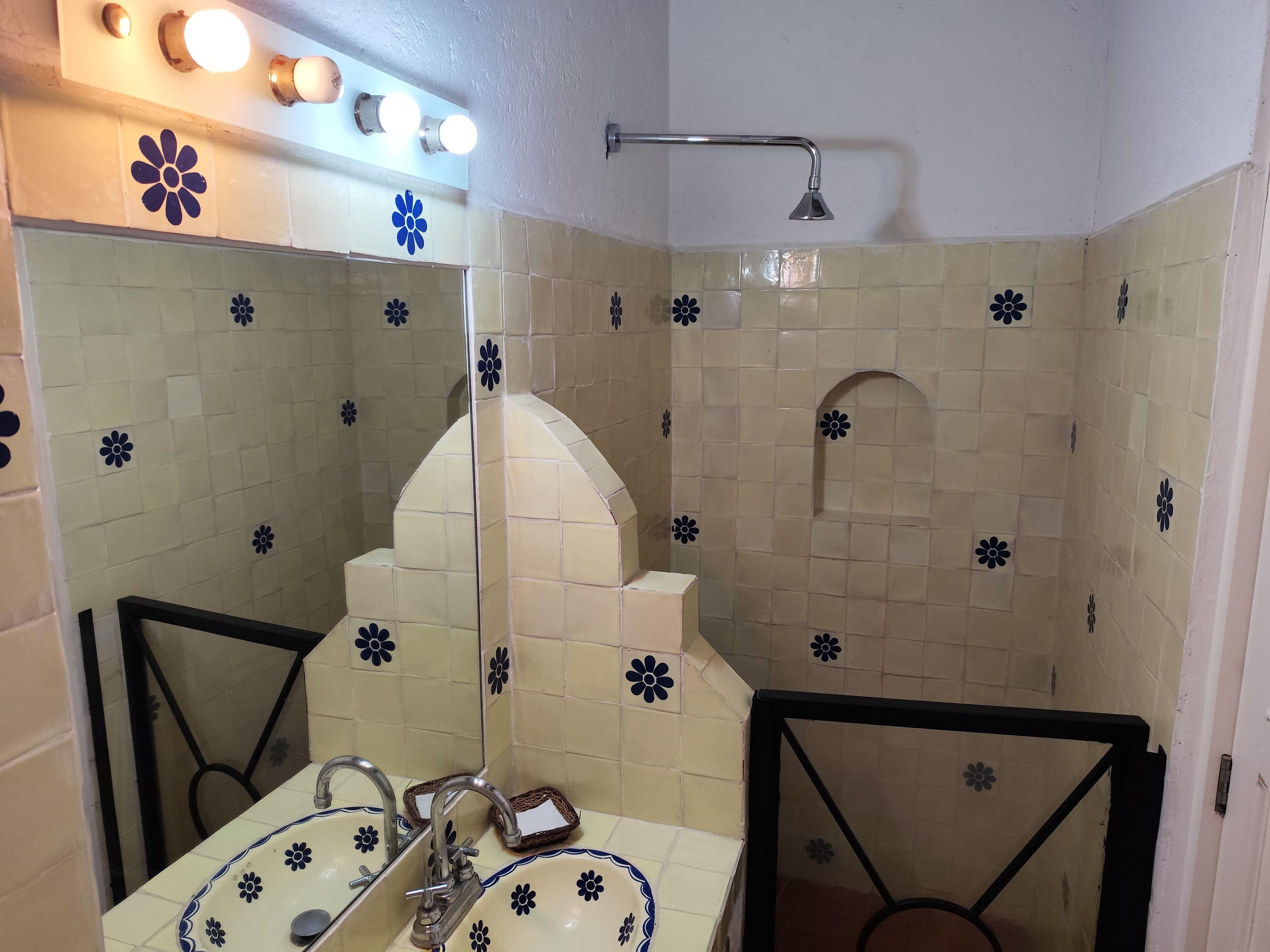 Un baño con lavabo, espejo y ducha. Las paredes están cubiertas de azulejos con un estampado floral.