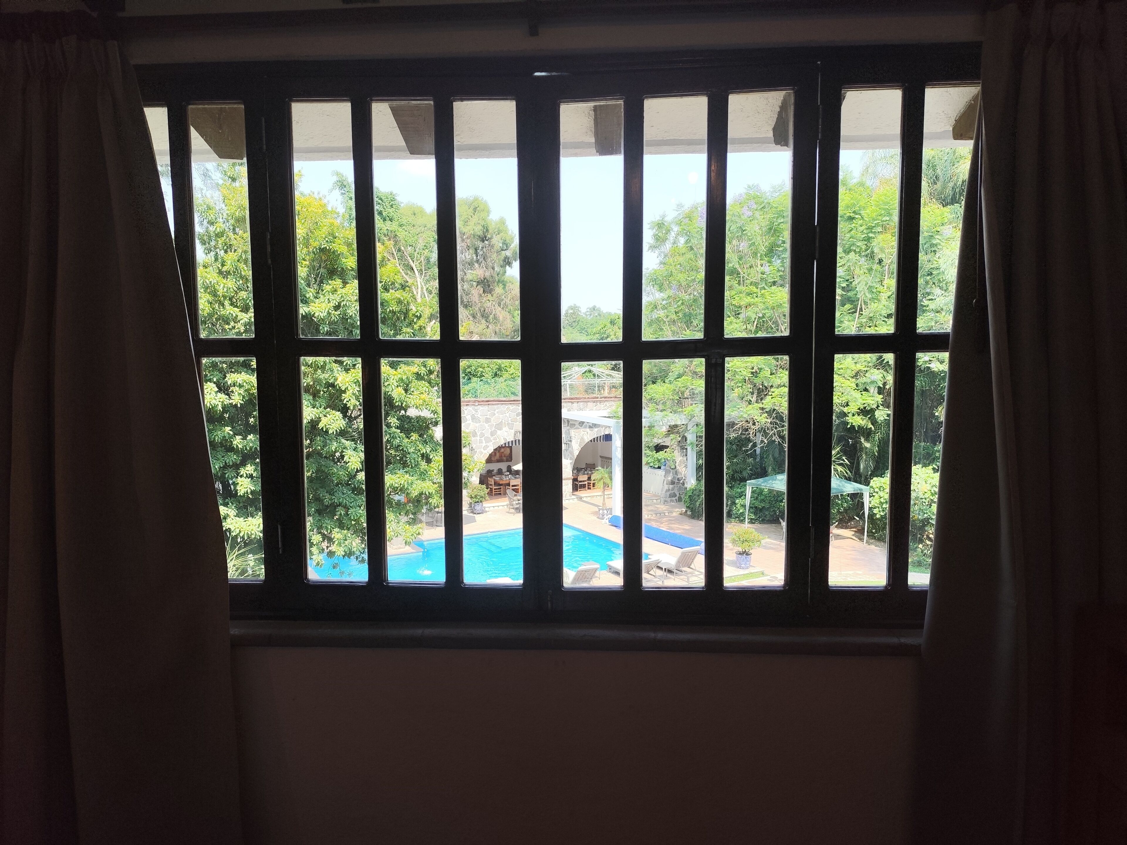 Janela com grades de metal, vista para uma piscina e vegetação lá fora.