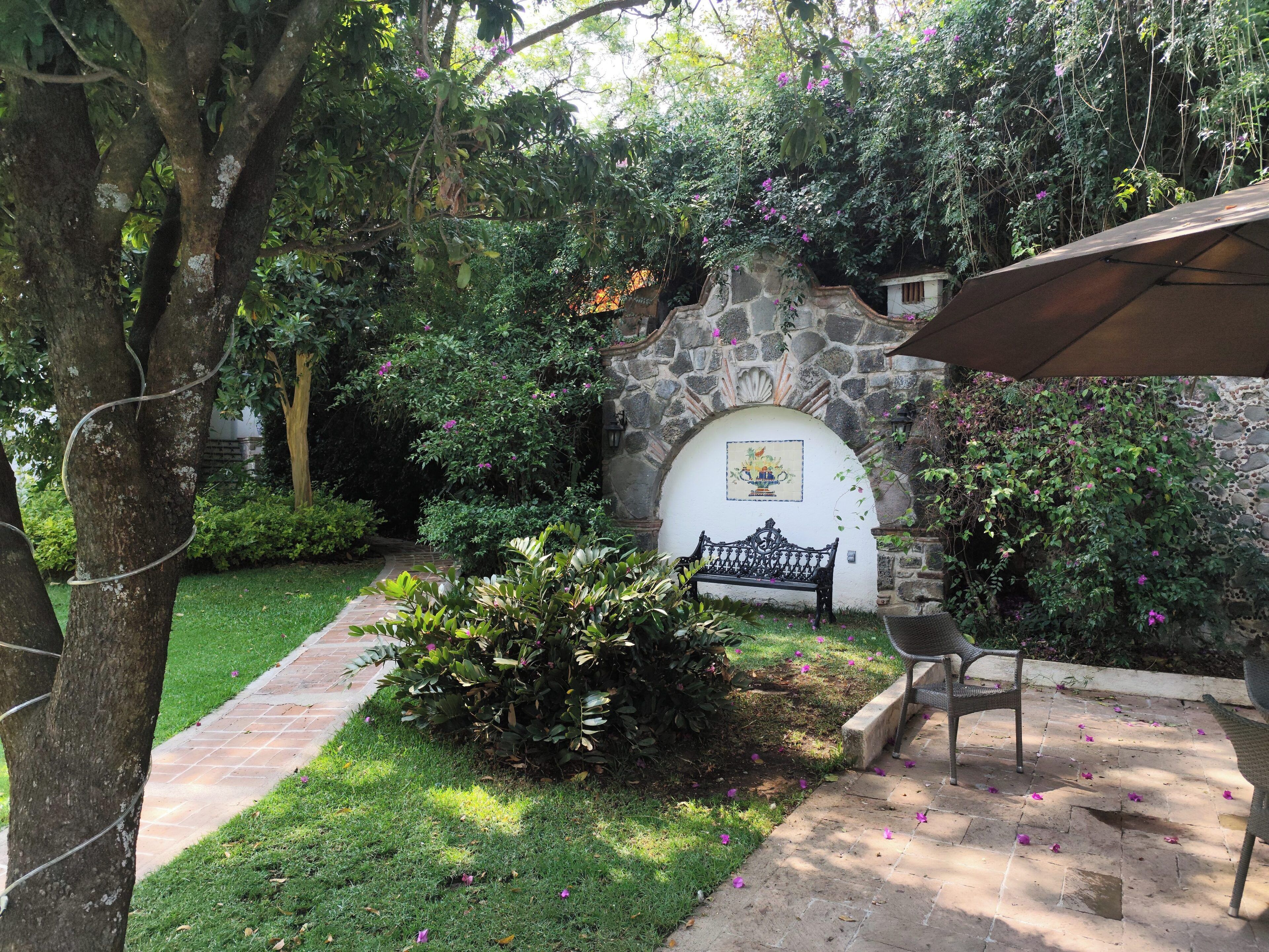 Un muro de piedra con un mural de azulejos, un banco y un jardín con un sendero.