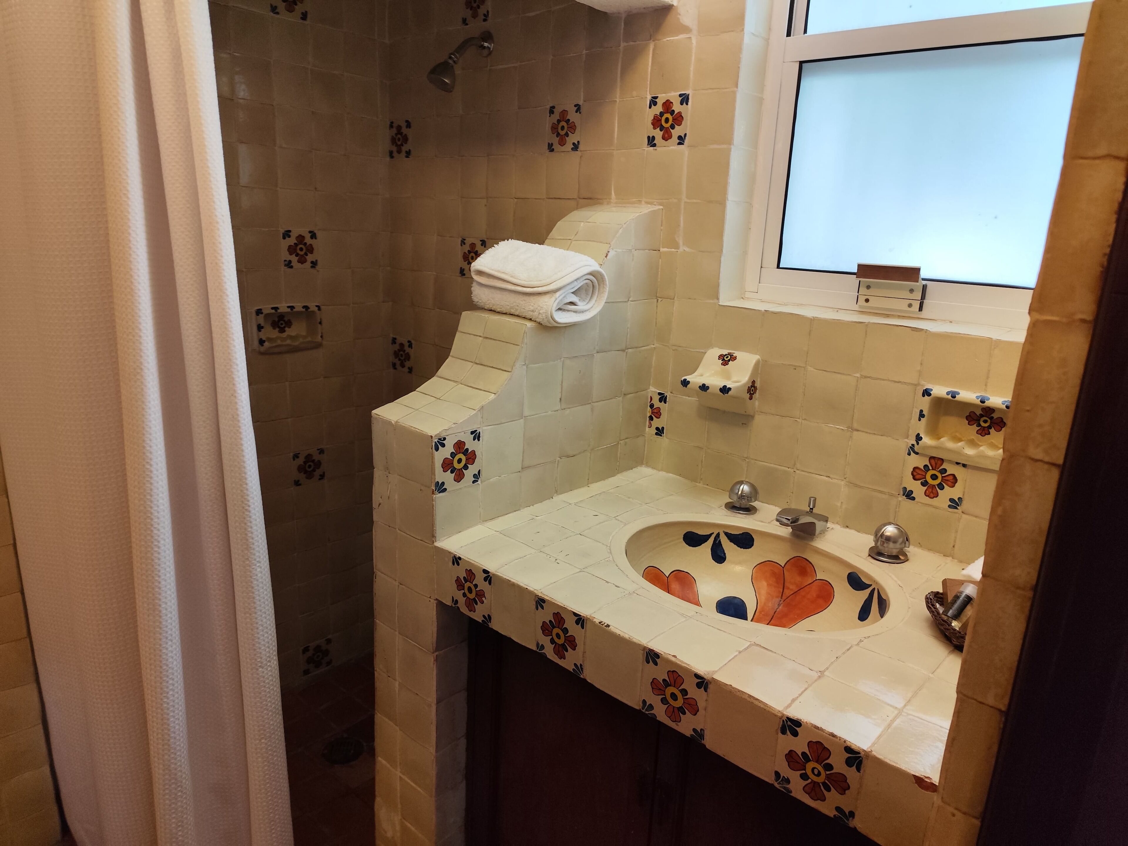 A bathroom with a sink, toilet, and shower. The walls are tiled with a floral pattern.