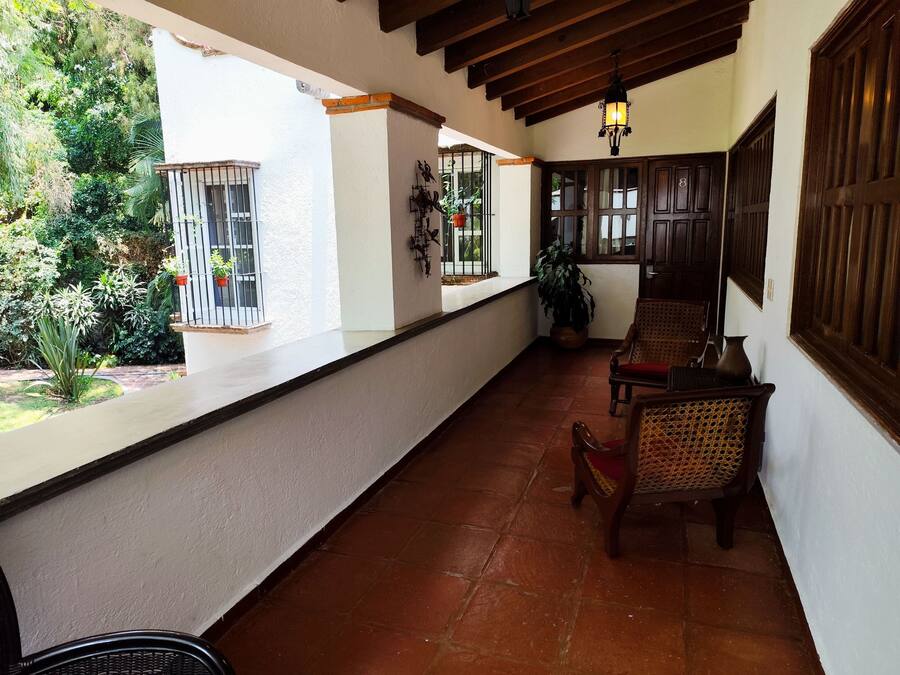 A covered patio with terracotta tiles, wooden furniture, and potted plants.