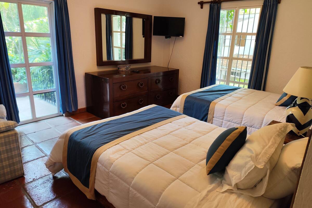 Quarto de hotel com duas camas, cômoda, televisão e vista para o exterior.