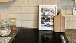 Een keuken met een zwart fornuis, een houten snijplank en een zwart-wit foto in een lijst op het aanrecht.