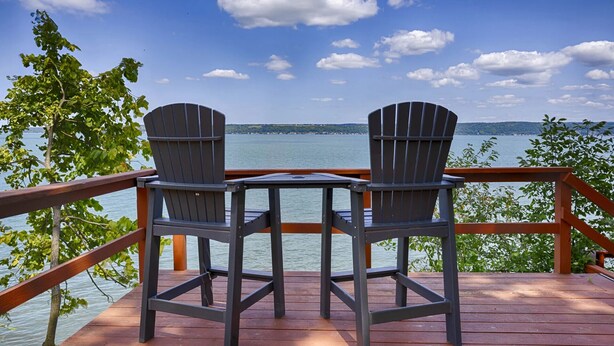 Eine Holzterrasse mit zwei Adirondack-Stühlen, die auf ein Gewässer ausgerichtet ist, umgeben von Bäumen.