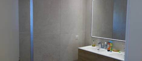 A modern bathroom with a large mirror, a sink, and a shower area.