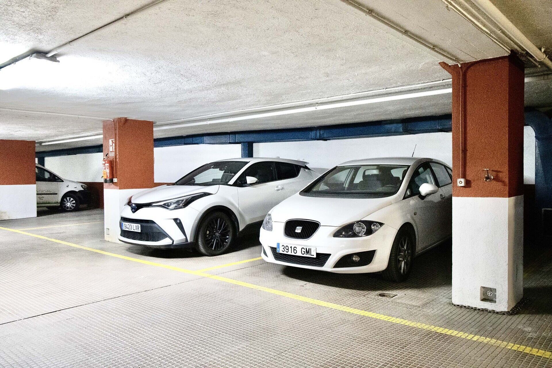 Un parking avec deux voitures blanches garées sous des piliers.