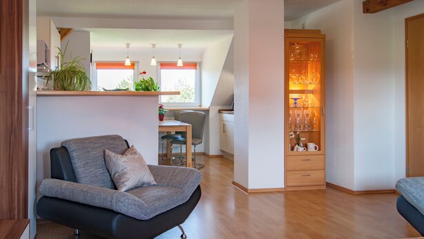 Una sala de estar moderna con un sofá de cuero negro, una mesa de comedor de madera y una zona de cocina con ventana.