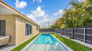 A swimming pool with a clear blue water, surrounded by a well-maintained lawn and a wooden fence.