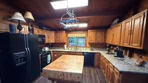 A kitchen with wooden cabinets, a black refrigerator, a wooden island, and a hanging light fixture.