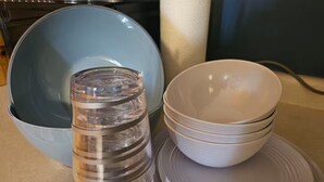 Un comptoir de cuisine avec une pile d’assiettes blanches, un récipient transparent en verre et un bol bleu.