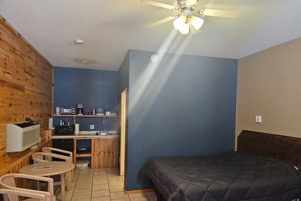 A compact room with a bed, a kitchenette, a small table with chairs, and a ceiling fan. - Barn In The Bush- Room 1, Lower level 2 queen beds (Russell)