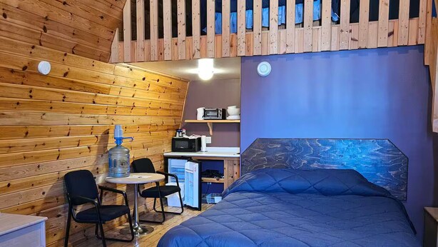 A cozy cabin-style room with a bunk bed, wooden walls, a small kitchenette, and a dining area. - Barn In The Bush - Room 4, King, queen & futon (Russell)