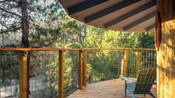 Una terraza de madera con barandilla metálica, una única silla Adirondack y vistas a un área boscosa.