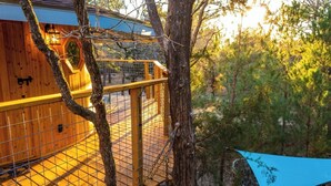 Une terrasse en bois avec une rambarde en métal, entourée d’arbres et surplombant un ciel bleu.