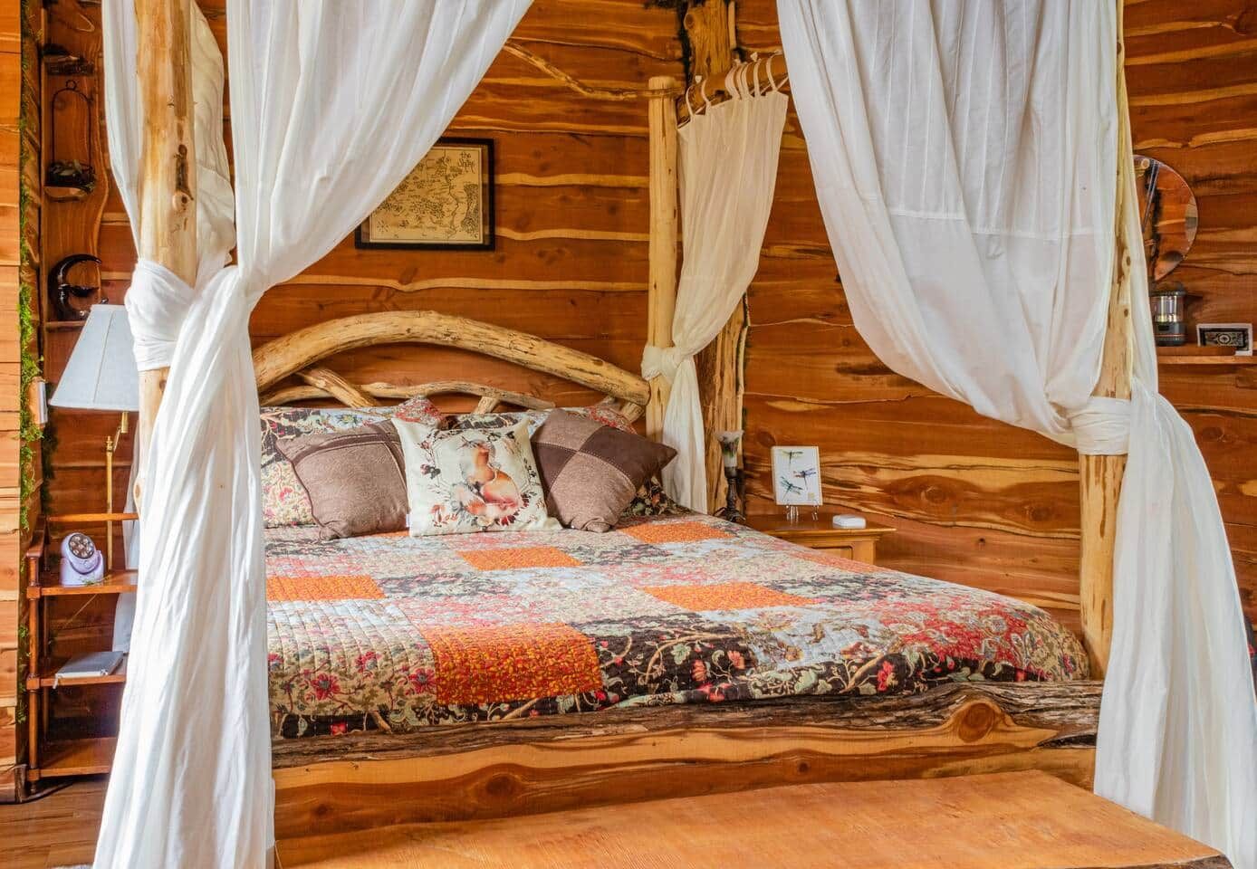 A wooden four-poster bed with a floral quilt, a nightstand with a lamp, and a framed map on the wall.