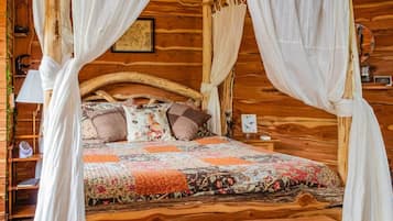 A wooden four-poster bed with a floral quilt, a nightstand with a lamp, and a framed map on the wall.