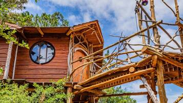 Una casa en el árbol de madera con un ventanal circular y una escalera de madera.