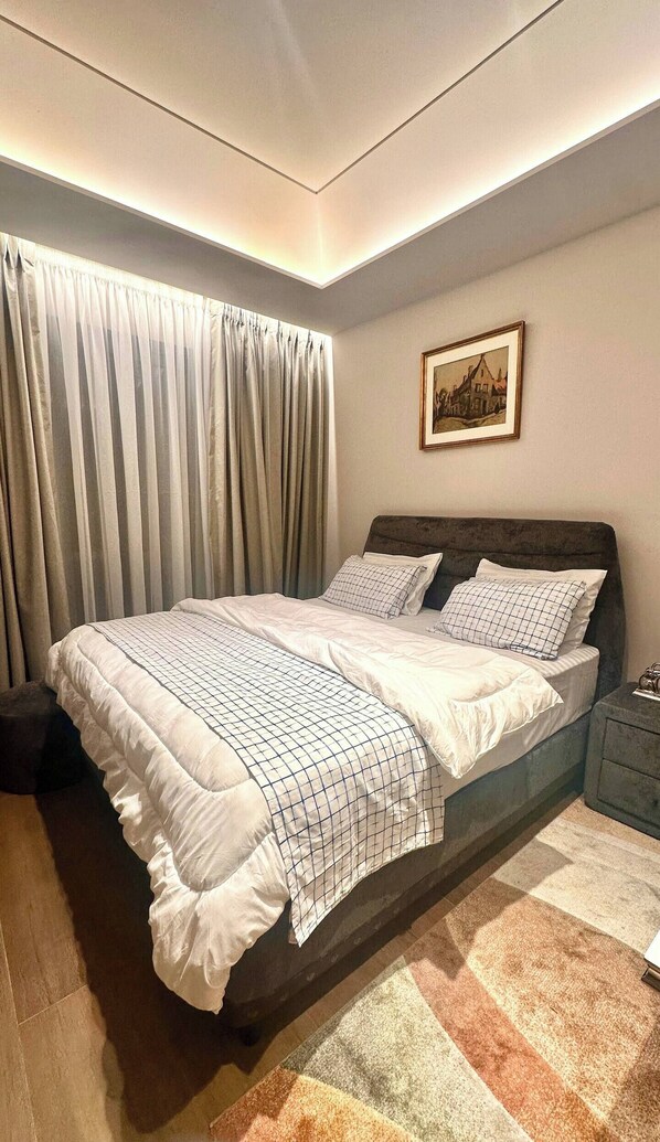 A bedroom with a large bed, a nightstand, a framed picture on the wall, and a window with curtains. - Studio apt. - Diamond in City (Accra)