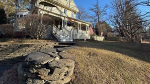 A two-story house with a porch, stone steps, and a flag.