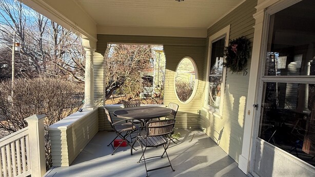 A covered porch with a table and chairs, a doormat, and a wreath on the wall.