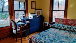 A bedroom with a bed, desk, chair, dresser, and windows.