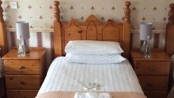 Un letto rifatto con lenzuola bianche, due comodini con lampade e carta da parati a motivi floreali.