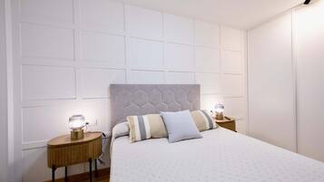 Een slaapkamer met een groot bed, twee nachtkastjes met lampen, een wit hoofdbord en een wandpaneel in wit design.