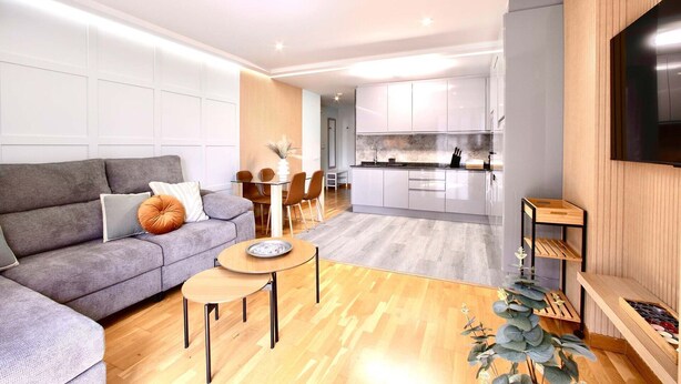 A modern living room with a grey sofa, a small round table, and a TV mounted on the wall. - Rosalia Park by Lugo Collection (Unknown)