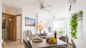 A dining area with a wooden table, chairs, and a fruit bowl. There is a ceiling fan, a painting on the wall, and a plant on the windowsill. - The Charm of Val-calm and sea views in Bolnuevo (Bolnuevo)