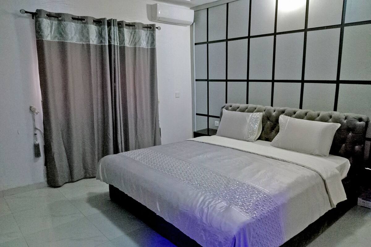 A bedroom with a bed, curtains, a headboard, and a tiled floor.