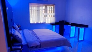 Une chambre à coucher avec un lit, des tables de chevet, une fenêtre avec des stores et un éclairage d’ambiance bleu.