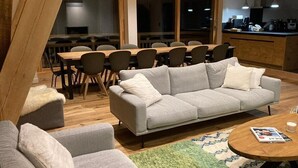 Uma sala de estar moderna com um sofá cinzento, uma mesa de centro de madeira e uma área de jantar com uma mesa grande e cadeiras.