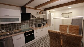 A modern kitchen with white cabinets, a microwave, a dishwasher, and a built-in oven. There are wicker chairs and a glass table. - Vacation home Weideblick (Geestland)