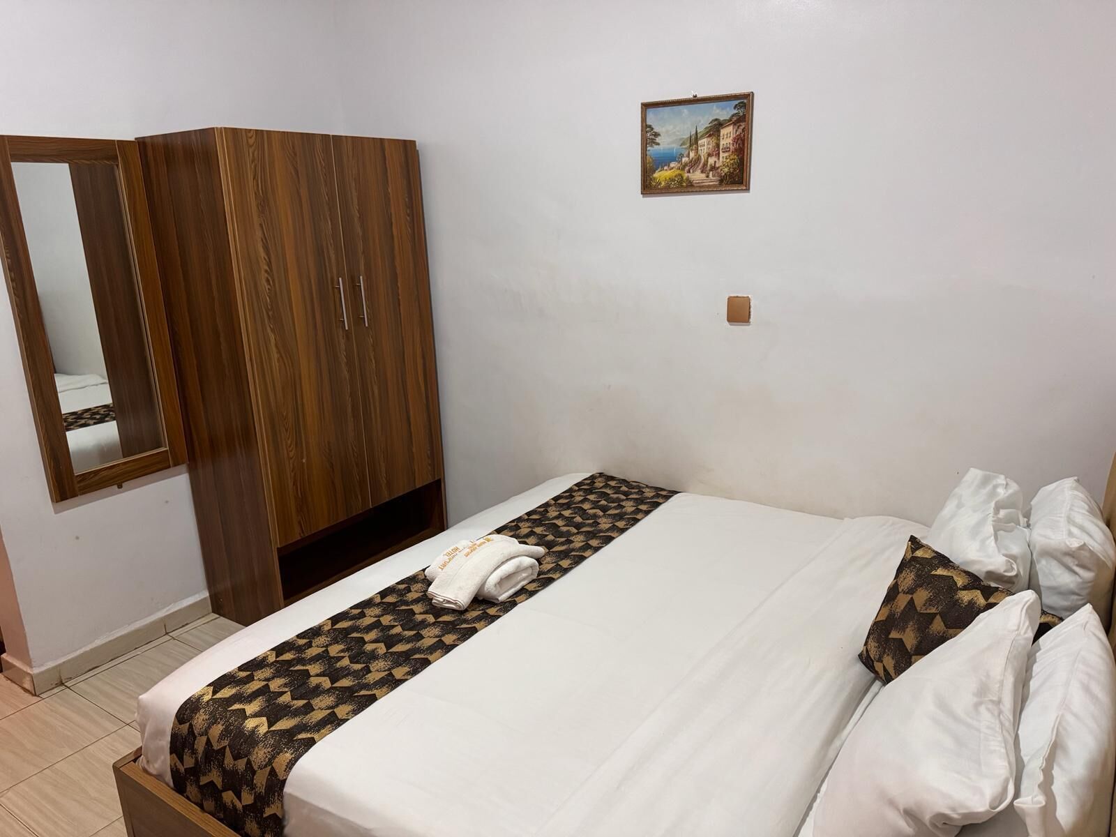A hotel room with a bed, a wardrobe, a mirror, and a painting on the wall.