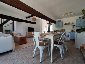 Un vaste espace de vie comprenant une table à manger, des chaises blanches, un canapé et un téléviseur.