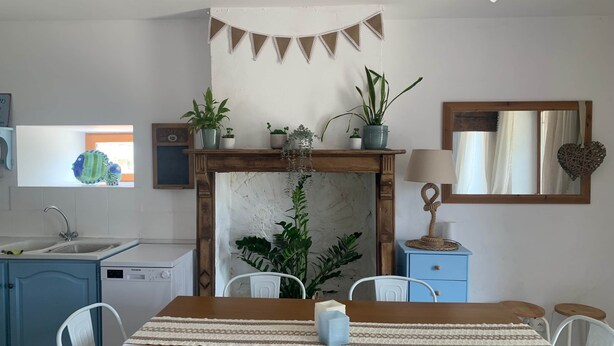 A kitchen with a wooden table, chairs, a sink, a stove, and various potted plants.