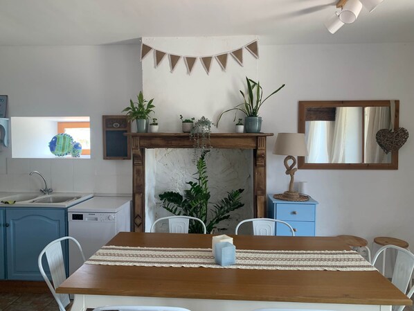 Een keuken met een houten tafel, stoelen, een spoelbak, een fornuis en verschillende potplanten.