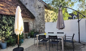 Eine Terrasse mit Tisch und Stühlen, einem weißen Sonnenschirm und einem hängenden Sonnensegel.