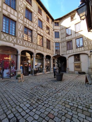 A courtyard with cobblestone flooring, a shop with mannequins, and a building with timber framing.