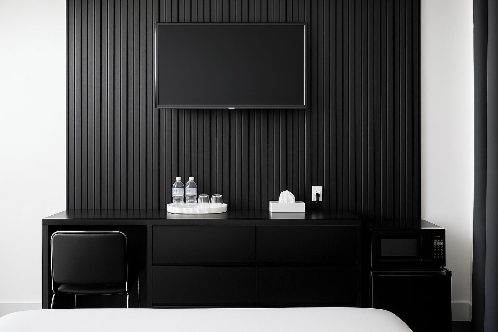 Ein modernes Hotelzimmer mit schwarzem Schreibtisch, einem Flachbildfernseher, einer Mikrowelle und einem Bett.