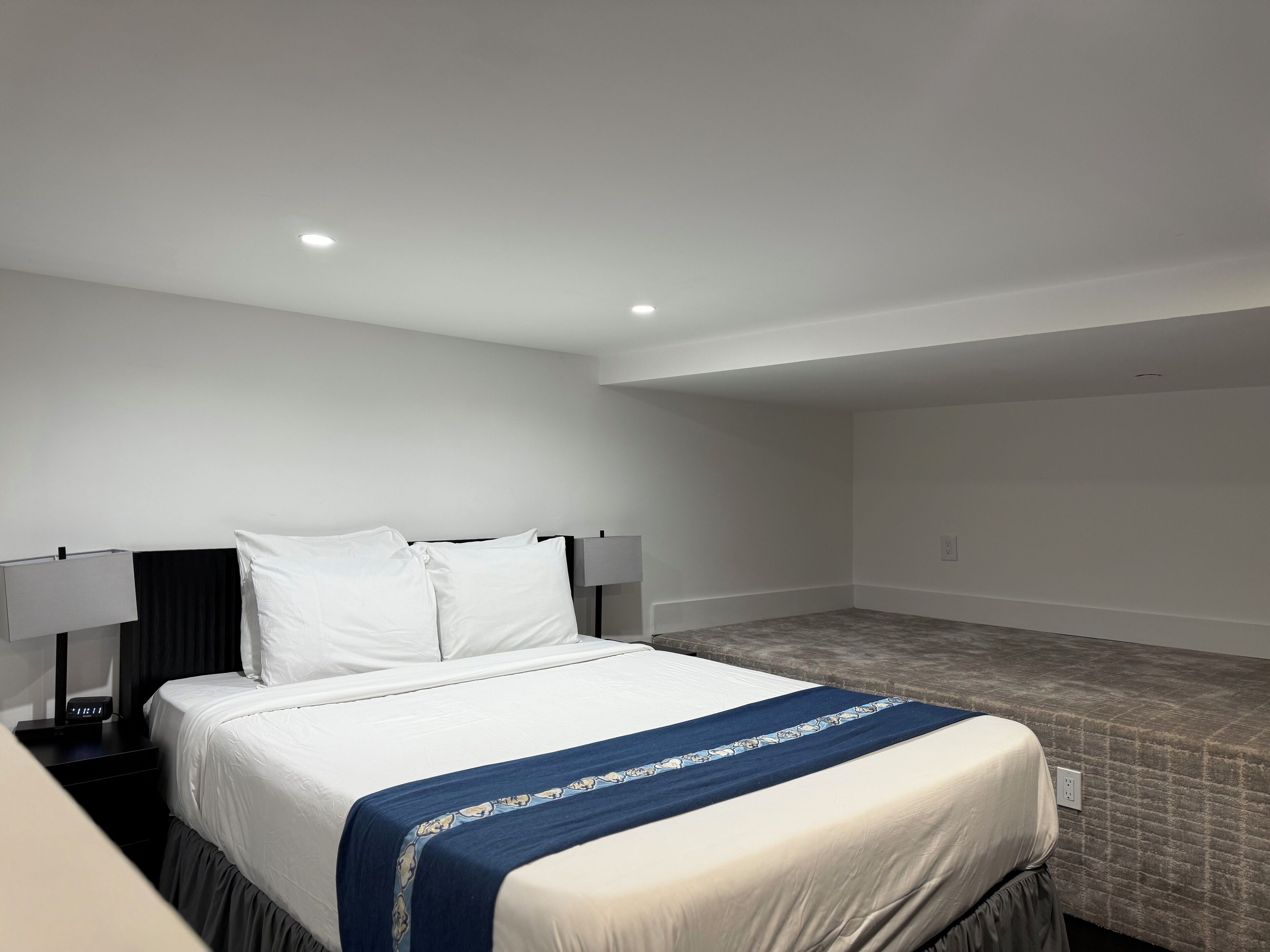 A hotel room with a bed, a nightstand, a lamp, and a tiled floor.